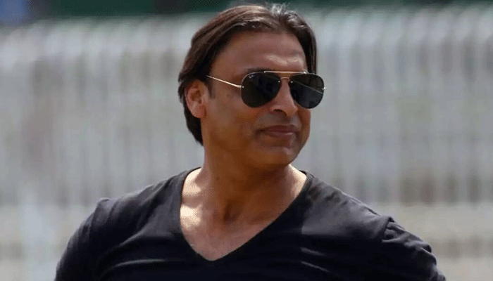 A close-up portrait of former Pakistani cricketer Shoaib Akhtar wearing sunglasses and a black v-neck shirt, looking to his right