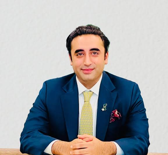 A portrait of Bilawal Bhutto Zardari, a Pakistani politician, wearing a dark blue suit and a patterned yellow tie, with a Pakistan flag pin on his lapel.
