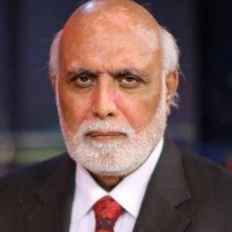 A portrait of a man with a white beard and a bald head, wearing a dark suit and a red patterned tie.
