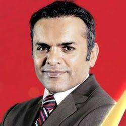 “Professional headshot of man in dark suit and striped tie against red background”