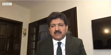 Pakistani journalist Hamid Mir in a formal portrait wearing a suit and white shirt against a plain background.