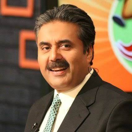 A portrait of Pakistani journalist and television host Aftab Iqbal, a middle-aged man with a mustache and graying hair, smiling while wearing a black suit and a patterned tie.