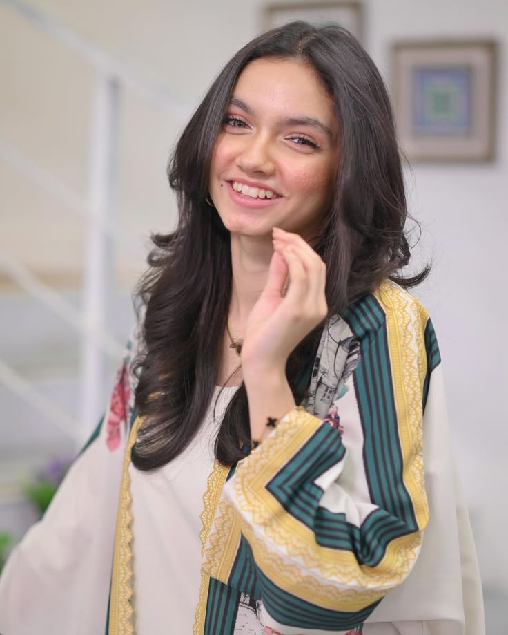 Aina Asif, a young Pakistani actress, smiling and wearing a white and green patterned outfit.