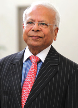 Dr. Ishrat Hussain, senior Pakistani economist, wearing a pinstripe suit and red tie in a professional portrait
