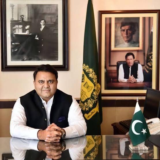 Fawad Chaudhry, a Pakistani politician, sits at his desk with portraits of Muhammad Ali Jinnah and Imran Khan behind him.