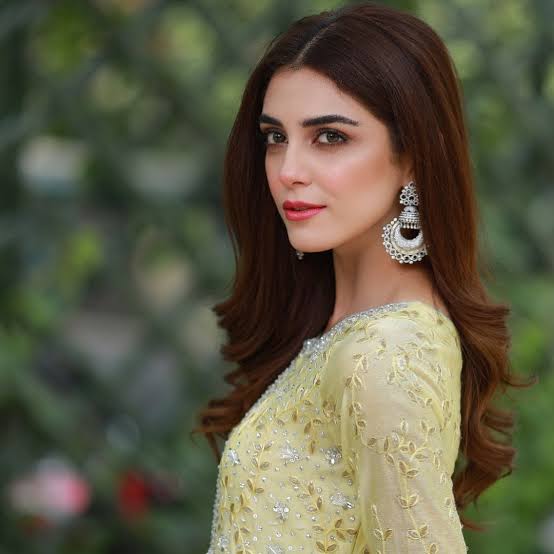 A portrait of Pakistani actress Maya Ali wearing a light yellow embroidered dress and large silver earrings.
