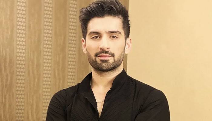A portrait of Pakistani actor Muneeb Butt. He is wearing a black shirt and a chain.