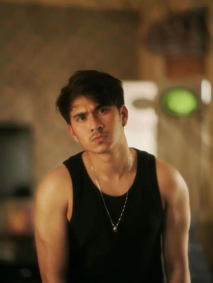 A close-up portrait of actor Samar Abbas Jafri, a young man with dark hair and a serious expression, wearing a black tank top and a silver chain.
