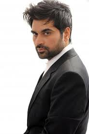 A headshot of Pakistani actor Humayun Saeed, who has dark hair and a beard, wearing a black suit and white shirt, looking over his shoulder at the camera.
