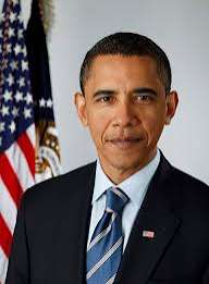 Official portrait photograph of Barack Obama in a dark suit and striped blue tie, standing in front of an American flag
