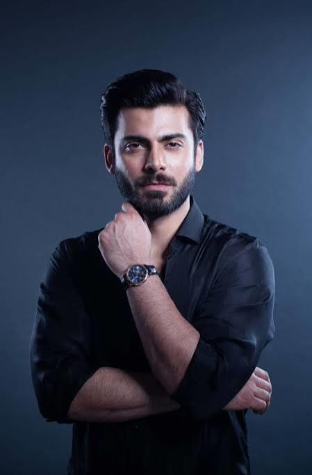 Portrait of Fawad Khan in a black shirt, looking at the camera with his hand on his chin.