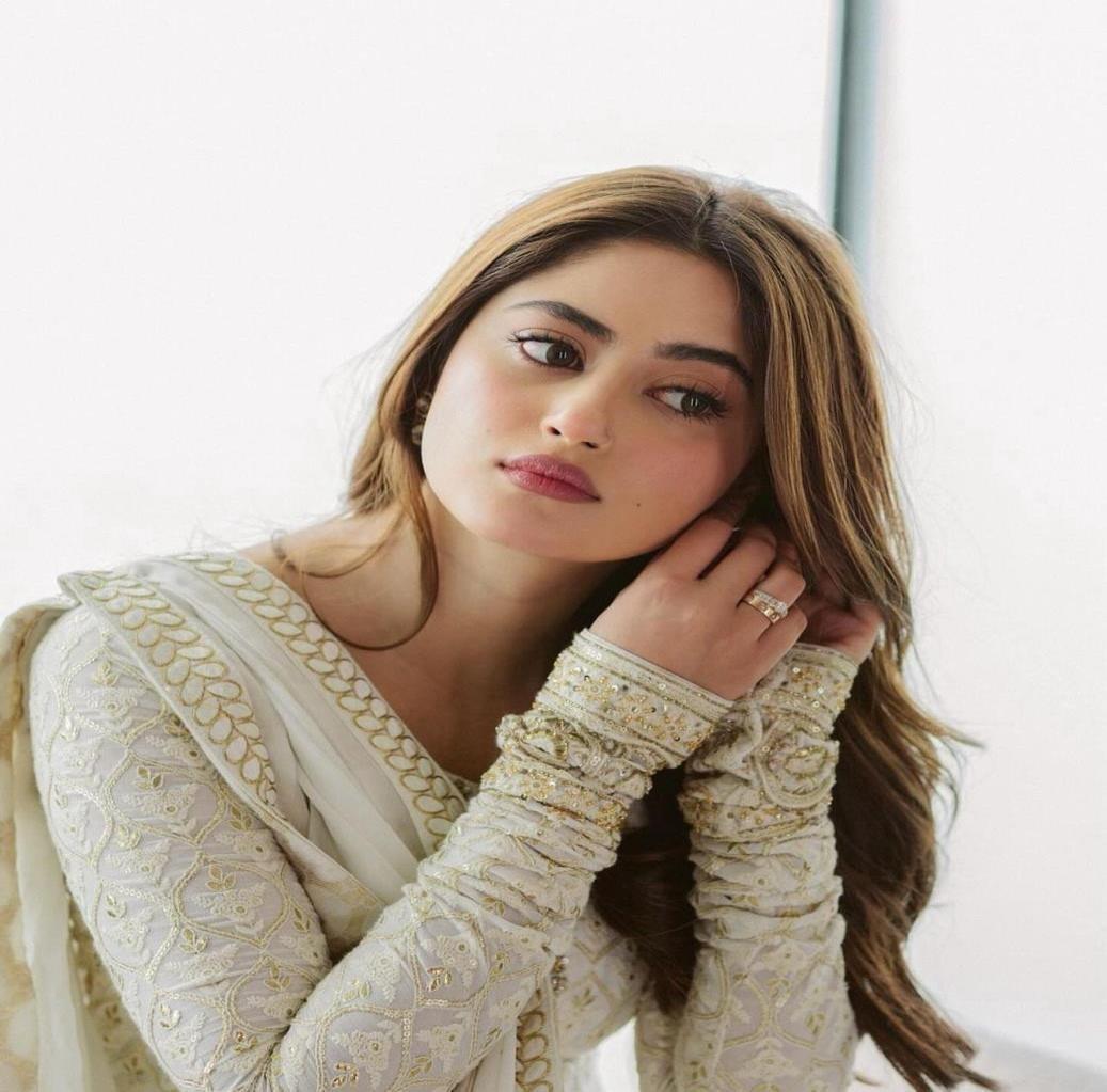 Sajal Aly in a white embroidered outfit, adjusting her earring.