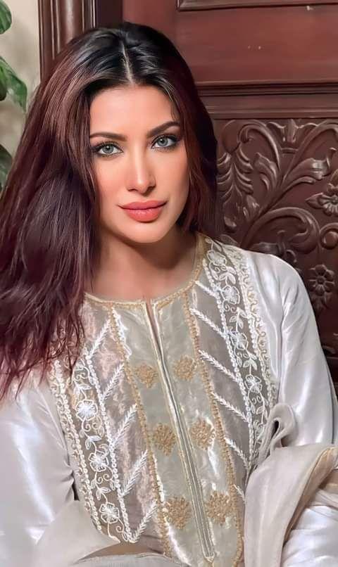 A close-up portrait of Pakistani actress Mehwish Hayat, with brown hair and light-colored eyes, wearing a white embroidered dress.