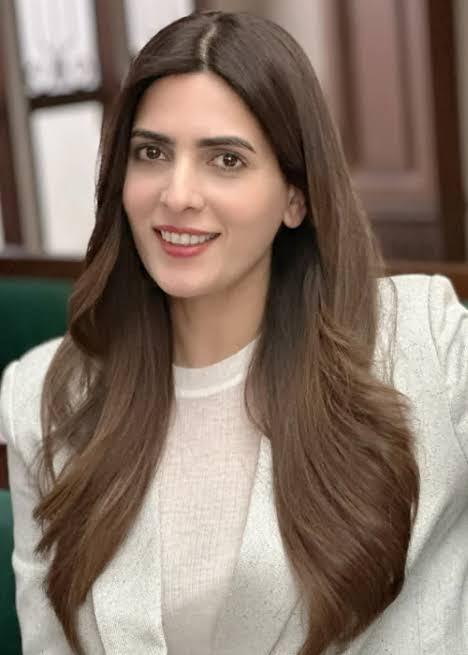 A headshot of a smiling woman with long brown hair, identified as Rushna Khan, wearing a light-colored blazer.