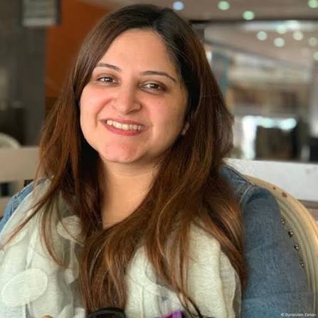 Maria Omer smiling confidently, wearing a necklace, half-face portrait