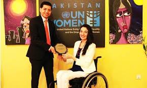 Muniba Mazari receiving an award on stage, seated in a wheelchair, smiling confidently while holding a trophy, dressed in elegant traditional attire.